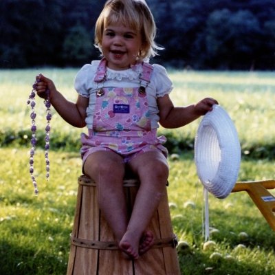 Childhood photo of BrandFuel employee Bridget Ray holding a hat and necklace.