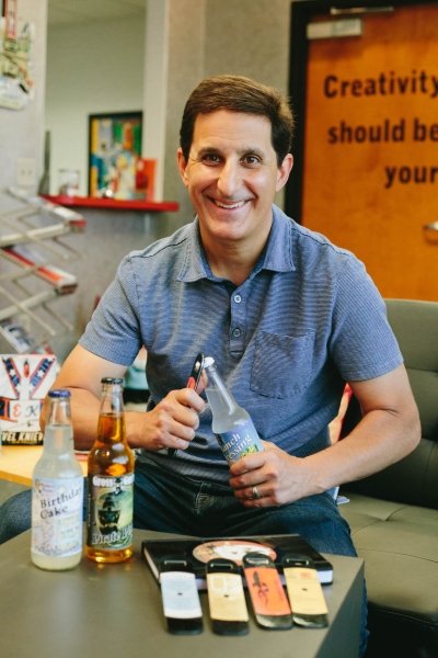 Photo of BrandFuel CEO Danny Rosin sitting down and opening a bottle.