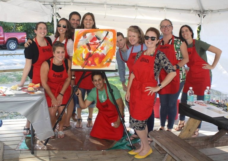 People posing next to a painting during a "Paint for Swag" event.