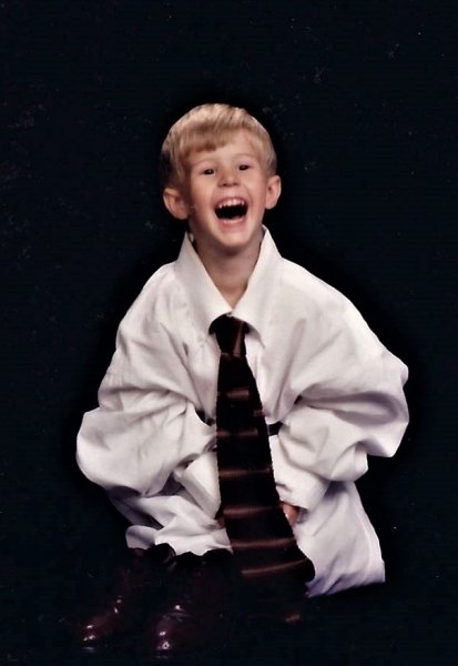 A young blake dressed in an an adult-sized dress shirt and tie.